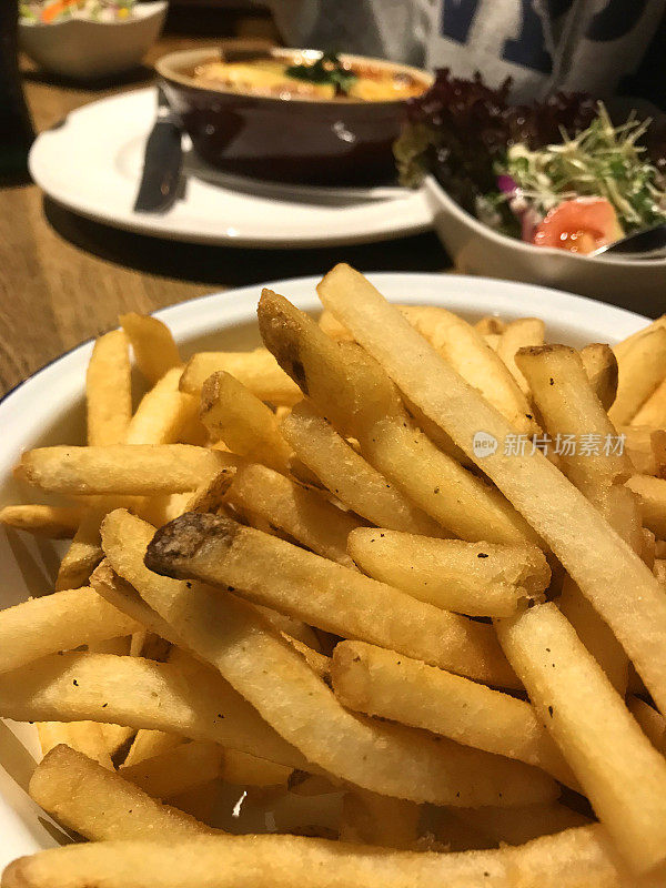 形象酥脆的大块薯条/法式炸薯条酒吧美食餐厅，不健康的吃薯条，法式炸薯条意大利餐千层面/千层面和配菜沙拉，油腻的小吃，随时可以吃的木制餐桌，盐和醋，番茄酱